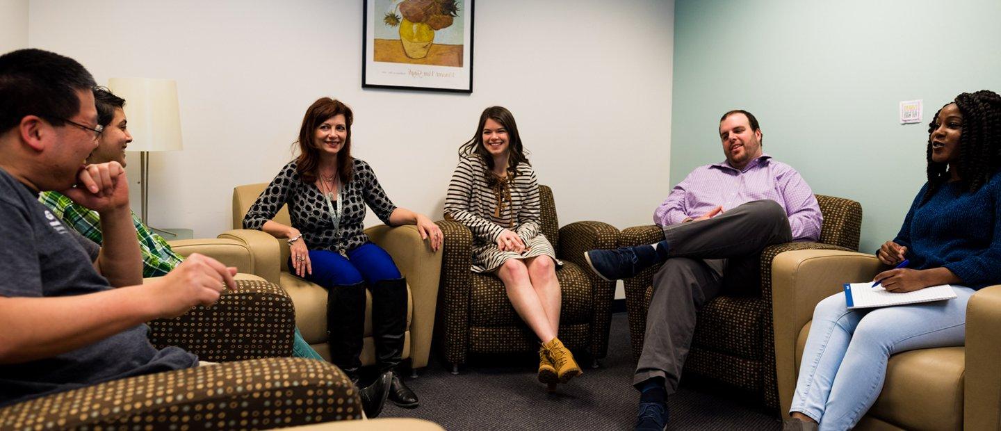 Six people seated in arm chairs, facing each other, smiling and talking.